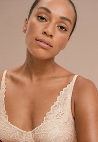 Blonde blonde bralette i blød beige med blomsterdesign, der har justerbare stropper og en dyb V-hals. Glat tekstur hele vejen igennem.