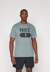 Grå bomulds t-shirt med et stort sort "NIKE 1" logo på forsiden. Rund halsudskæring og korte ærmer. Båret med sorte shorts.