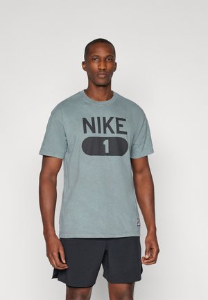 Sivi pamučni majica s velikim crnim logotipom "NIKE 1" sprijeda. Okrugli izrez i kratki rukavi. Nositi s crnim kratkim hlačama.
