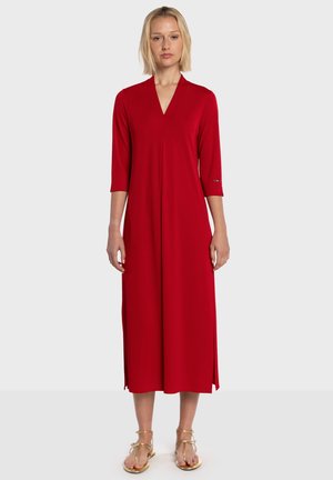 Robe rouge mi-longue avec col en V et manches trois-quarts. Tissu doux, deux fentes latérales, détails minimalistes en métal.