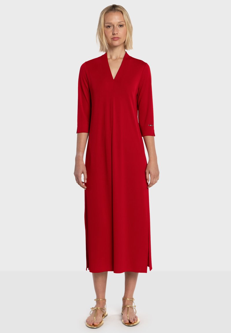 Robe rouge mi-longue avec col en V et manches trois-quarts. Tissu doux, deux fentes latérales, détails minimalistes en métal.