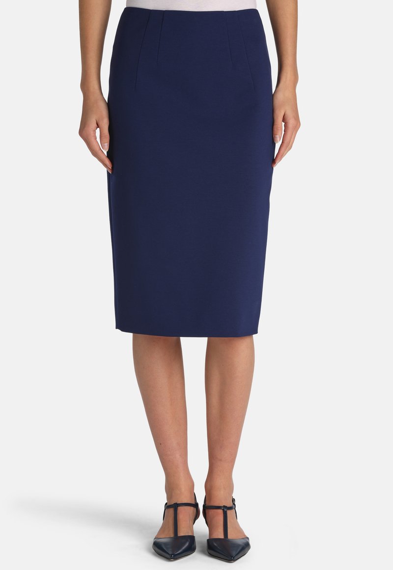 Woman wearing a navy blue knee-length pencil skirt and black T-strap pointed-toe heels, standing against a plain background.