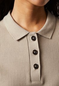 Beige ribbet polo-shirt med en knaplukning med tre mørke knapper og en blød, tekstureret krave.