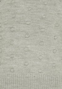 Pull en maille vert clair présentant une surface texturée avec des motifs circulaires en relief et un ourlet côtelé. Tissu doux de poids moyen.