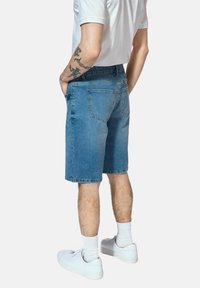 Jasnoniebieskie szorty dżinsowe o regularnym kroju, z przeszytymi tylnymi kieszeniami i prostym wykończeniem. Noszone z białymi trampkami i skarpetkami do kostek.