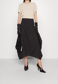 Beige kortærmet top, sort højtaljet nederdel med en svajende design, sorte læderhandsker og sorte spidse højhælede sko.
