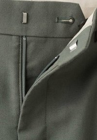 Pantalones verde oliva con un tejido texturizado, cierre de cremallera y un gancho de metal en la cintura para el ajuste.