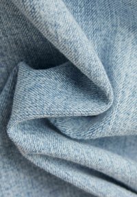 Light blue denim fabric, showcasing a soft, textured surface with distinct weaving patterns and gentle folds.