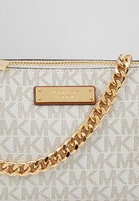 Sac à main beige Michael Kors avec motif MK répété, fermeture éclair dorée, plaque logo rectangulaire et épais bracelet à chaîne dorée.
