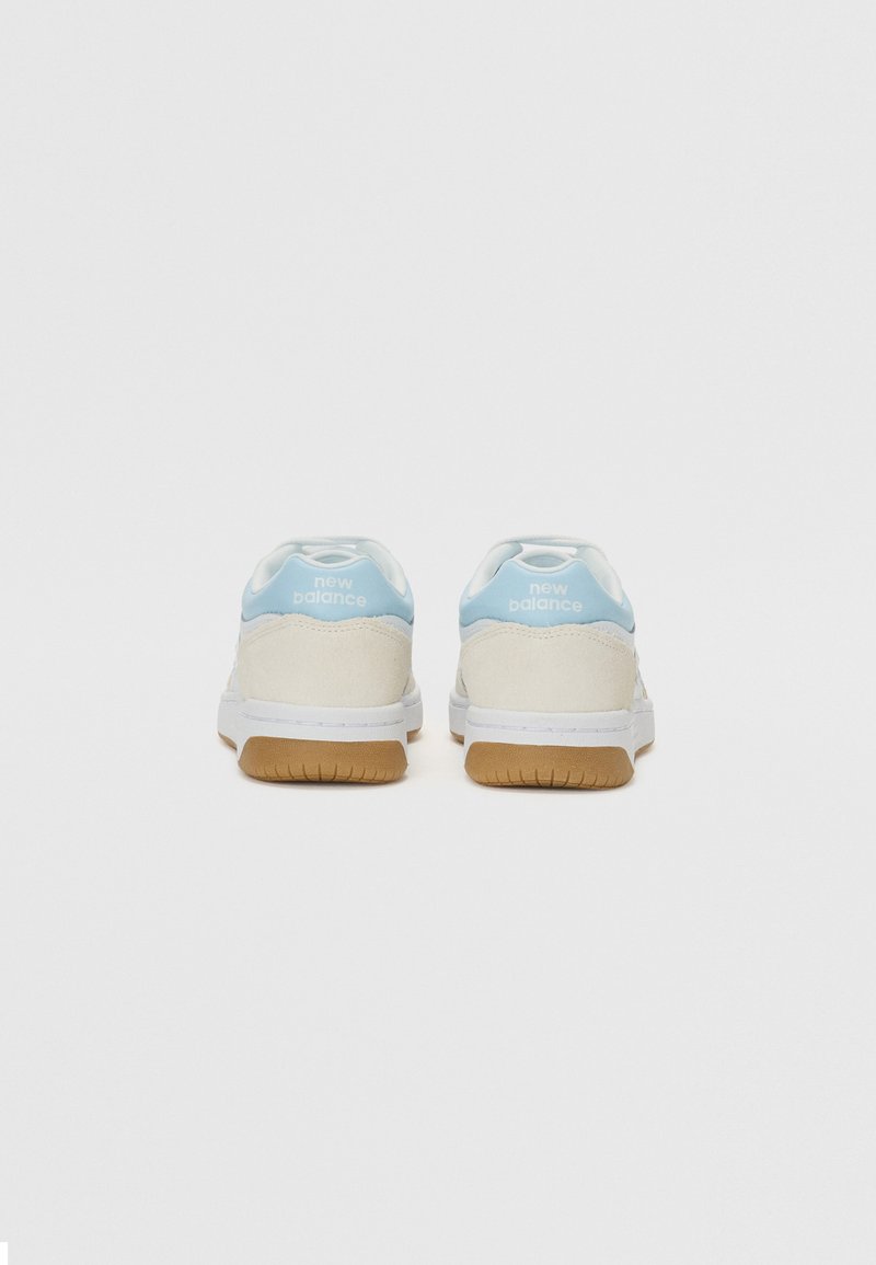 Zapatillas blancas con acentos azules claros, de materiales de ante y cuero, forma redondeada y suela de goma. Logo de "New Balance" en el talón.
