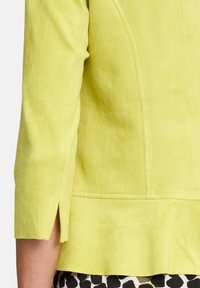 Limonkowa kurtka o miękkiej, teksturowanej powierzchni, z rękawami trzyczwartowymi i lekko rozkloszowanym dołem.