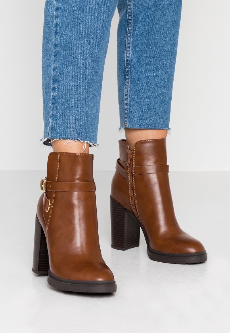 Hnědé kotníkové boty z kůže se zaoblenou špičkou, širokým podpatkem, bočním zipem a ozdobným páskem se zlatou přezkou.