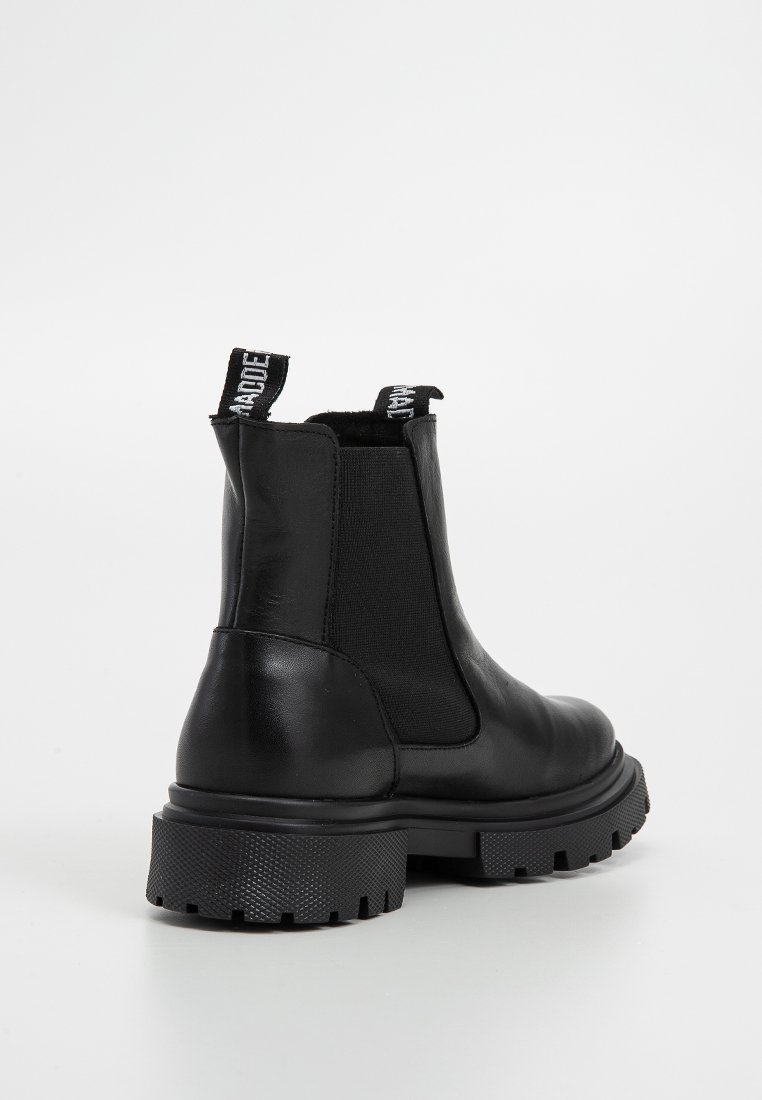 Stivale alla caviglia in pelle nera con suola spessa a ragno, pannello laterale elastico e linguette in tessuto con testo bianco.