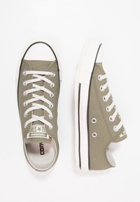 Baskets en toile vert olive avec semelles en caoutchouc blanc, bout rond et lacets blancs. Comprend des œillets et un patch logo sur la languette.