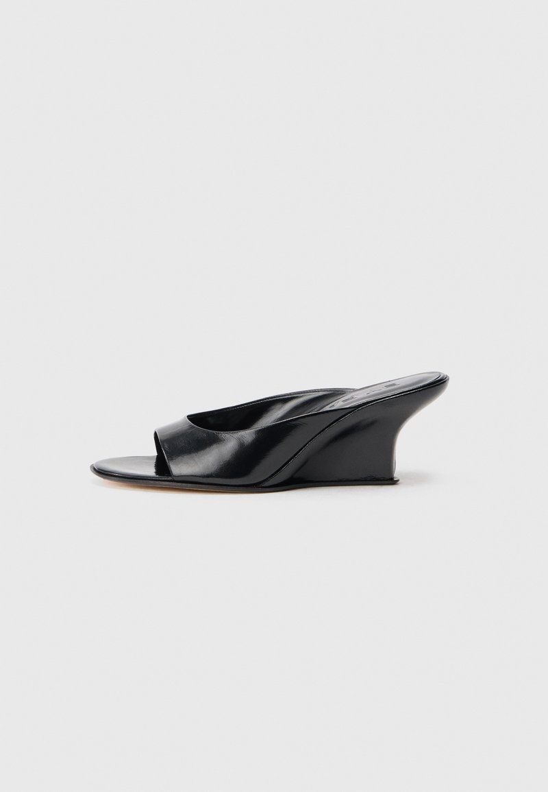 Black leather wedge sandals with an open toe, curved design, and smooth texture. Spanning a low wedge heel for subtle elevation.