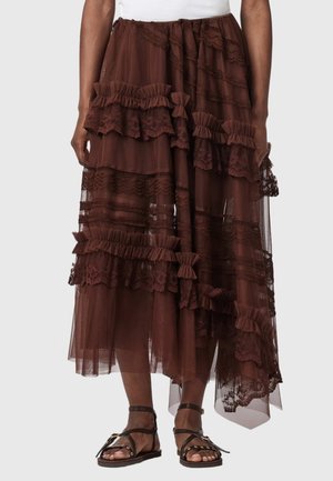 Jupe midi asymétrique marron avec des détails en dentelle superposée et des volants, portée avec des sandales plates noires à lanières.