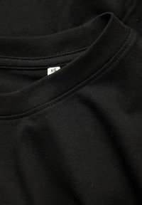 Čierne bavlnené tričko s okrúhlym výstrihom a viditeľnou štítkou s veľkosťou XS vo vnútri goliera.