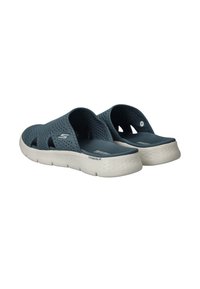 Blauwe instapsandalen met een gestructureerde bovenkant en een gewatteerde witte zool met een uniek patroon. Logo zichtbaar aan de zijkant.