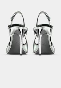 Ασημένια σανδάλια με ψηλό τακούνι και απαλό μεταλλικό φινίρισμα, ανοιχτή πλάτη, ρυθμιζόμενο λουράκι στον αστράγαλο και γυαλιστερό ασημένιο τακούνι.