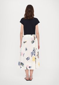 Topp med marineblå ermer uten skuldersøm parret med en hvit midiskjørt med blomsterdesign, som har flerfargede botaniske mønstre. Modellen har på seg sandaler med stropper.