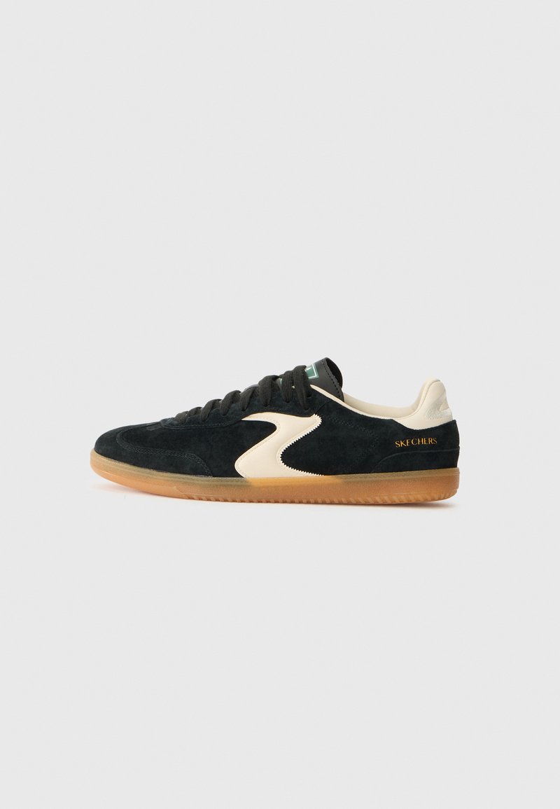 Black suede sneakers with a cream accent and gum sole. Features flat laces, a rounded toe, and "SKECHERS" printed in gold on the heel.