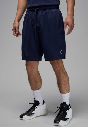 Man wearing navy athletic shorts with drawstring, white crew socks, and black-and-white basketball sneakers, standing on a gray floor.