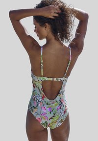 Costume da bagno intero floreale in grigio chiaro, con schiena bassa, spalline sottili e un motivo di piante colorato con accenti di rosa e verde.