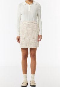 Witte geribbelde lange mouwen polo met een kraaghalslijn, gecombineerd met een textuur geweven mini rok in crèmekleurige en lichtoranje tinten.