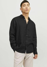Camisetta nera a maniche lunghe in lino con colletto a bottoni e una sottile texture. Presenta cinque bottoni lungo la parte anteriore.