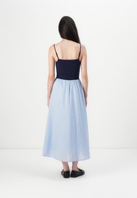 Cuerpo ajustado azul marino con tirantes finos, que se transforma en una falda maxi a rayas azul claro, usada con zapatos planos negros.