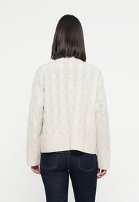 Maglione a coste color crema con design corto, bordo a coste e maniche lunghe, mostrato da dietro.