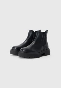 Botas Chelsea de cuero negro con suela gruesa, paneles laterales elásticos y tiradores para facilitar su puesta. Textura suave y diseño sencillo.