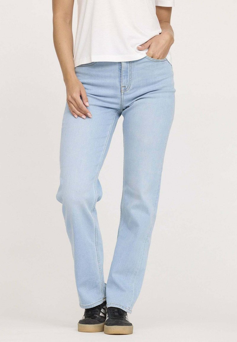 Jean en denim bleu clair avec une coupe droite, style cinq poches et détails de couture visibles, associés à des baskets noires.