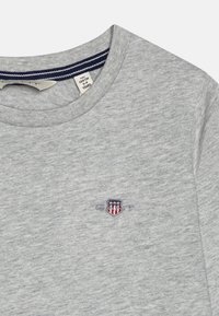 Grå bomull T-skjorte med rund hals, med en liten brodert logo i rødt, hvitt og blått på venstre side.