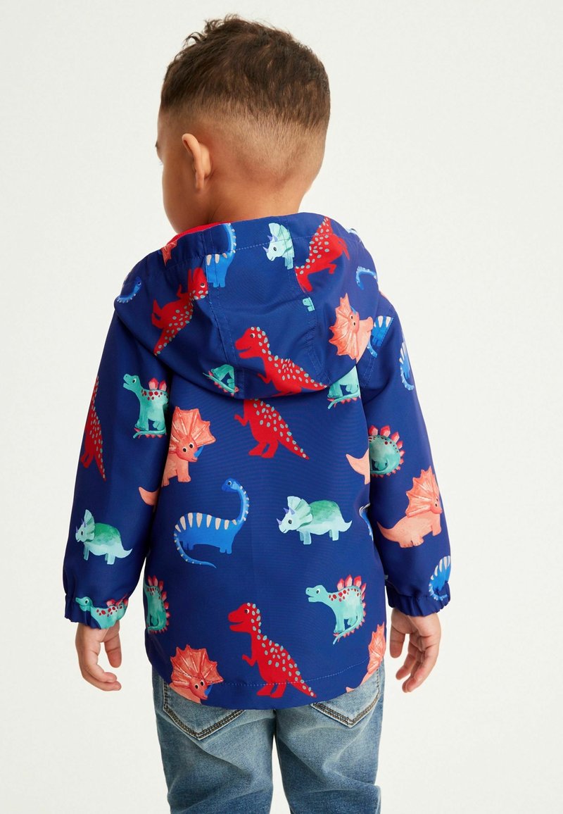 Veste légère bleue avec des motifs de dinosaures en rouge, vert et couleurs pastel. Elle est dotée d'une capuche et de poignets élastiques. Design décontracté.
