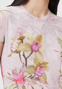 Průhledná blůza s květinovým potiskem obsahující r�ůžové a zelené orchideje, kulatý výstřih a krátké rukávy, vyrobená z lehkého, jemného materiálu.