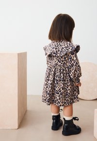 Leopardmuster Kleid mit gerafftem Kragen, beige und schwarze Farben. Kombiniert mit schwarzen Lackstiefeln und cremefarbenen Socken.