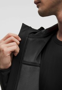 Svart jacka i mjukt tyg med dragkedja och ett innerfack. Släthet på utsidan med en strukturerad foder som syns inuti.
