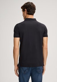 Zwarte polo met korte mouwen en een klassieke kraag, met een gladde textuur en een rechte pasvorm, gecombineerd met blauwe denim jeans.