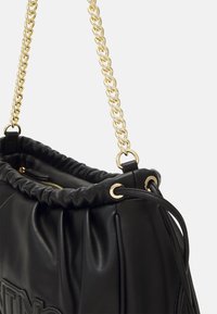 Bolso de mano de cuero negro con detalles fruncidos, correa de cadena dorada y cierre con cuerda, sobre un fondo blanco liso.