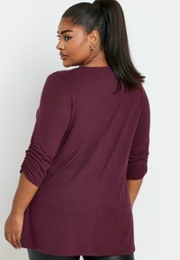 Maglietta a maniche lunghe color bordeaux con scollatura rotonda, maniche arricciate e orlo dritto, realizzata in un tessuto morbido e elasticizzato.