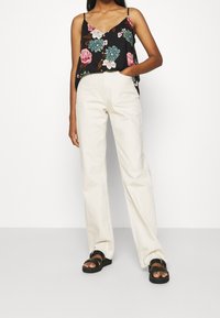Top de tirantes negro con estampado floral y escote en V, que presenta flores rosas y azules. Combinado con pantalones de pierna ancha beige claros y sandalias negras.