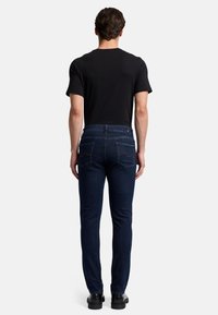 Jeans in denim blu scuro con una vestibilità slim, dotati di tasche posteriori e dettagli di cucitura. Abbinati a una camicia nera a maniche corte.