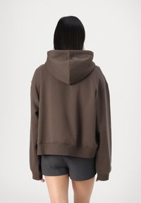 Sudadera corta marrón hecha de una tela suave, con capucha, mangas anchas y dobladillo acanalado. Presenta un ajuste relajado y costuras mínimas.