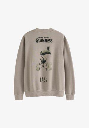 Vaaleanbeige collegepaita, jossa on toukankuvio ja teksti "Ihana päivä GUINNESSille" sekä resorit kauluksessa ja helmassa.