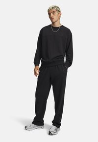 Zwarte sweatshirt en bijpassende broek van zachte stof. De sweatshirt heeft een ronde hals en een subtiel merklogo. Schoenen zijn zilveren sportieve modellen.