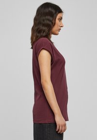 T-shirt bordeaux a maniche corte con vestibilità morbida, scollo rotondo e tessuto di cotone morbido. Vista laterale, con dettagli sui polsini arrotolati.