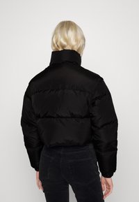 Sort dunjakke med høj krave og quiltet tekstur, med et kort snit og elastiske manchetter, båret med mørke fløjlsbukser.