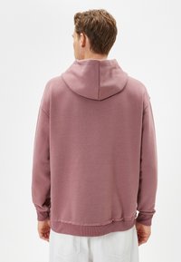 Rosa hoodie med ficka, långa ärmar och dragsko i huvan. Mjuk textur med fransig kant. Inga synliga logotyper eller mönster.