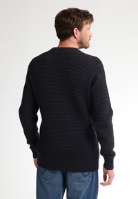 Marineblauwe gebreide trui met een ronde hals en geribbelde manchetten, met een normale pasvorm en een horizontaal patroon, gedragen met blauwe jeans.